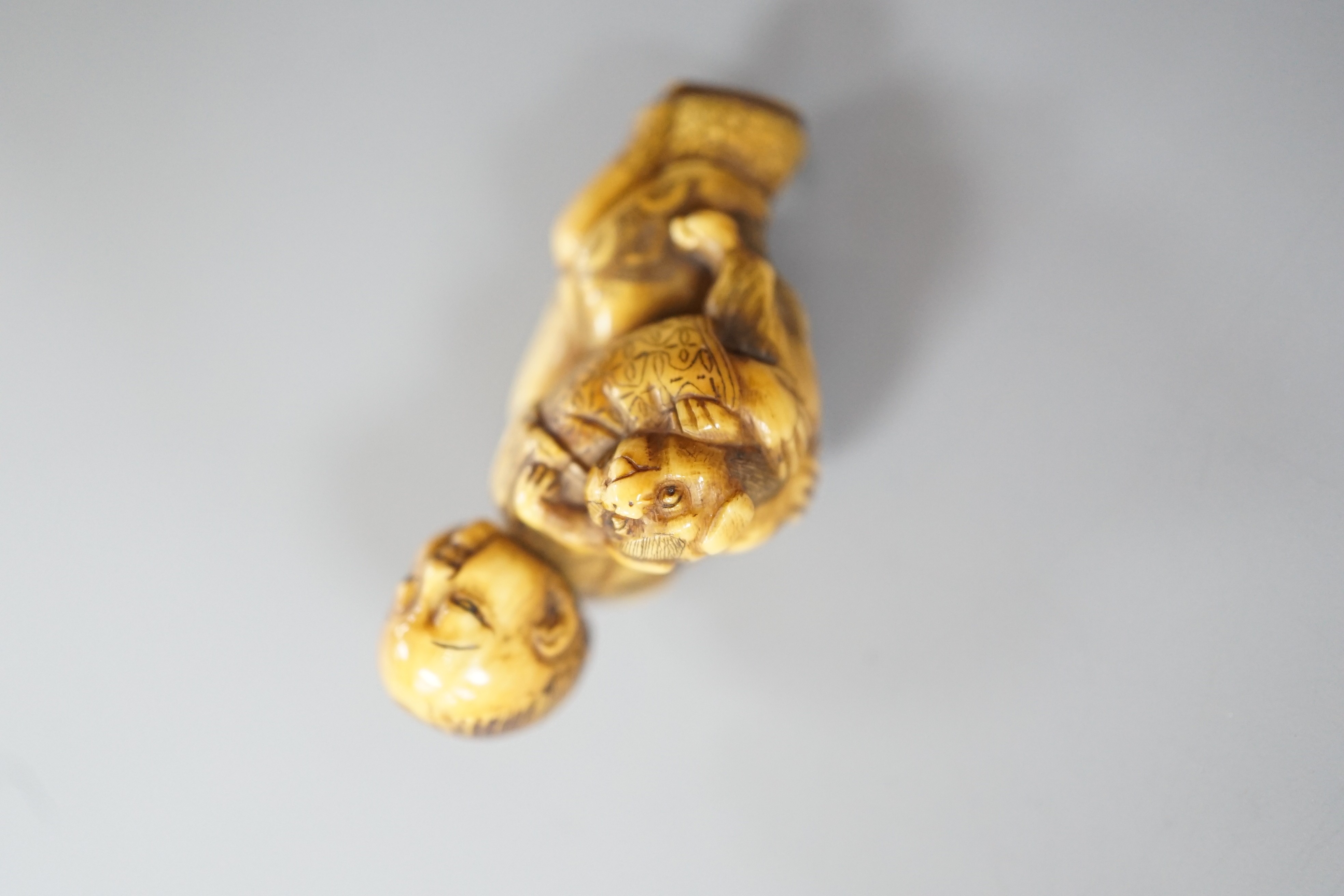 A Japanese ivory netsuke of a dog piggybacking a boy, Meiji period, 3.9cm